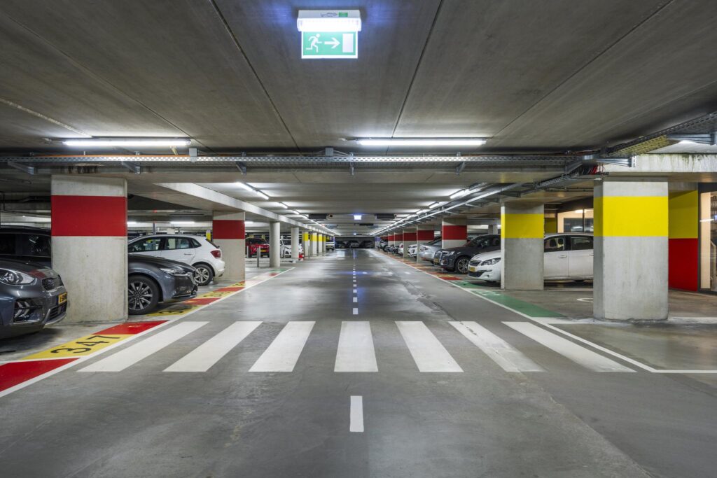 Overzicht van een goed verlichte, ondergrondse parkeergarage aan de Laan van de Helende Meesters met geverfde rijstroken en parkeervakken.